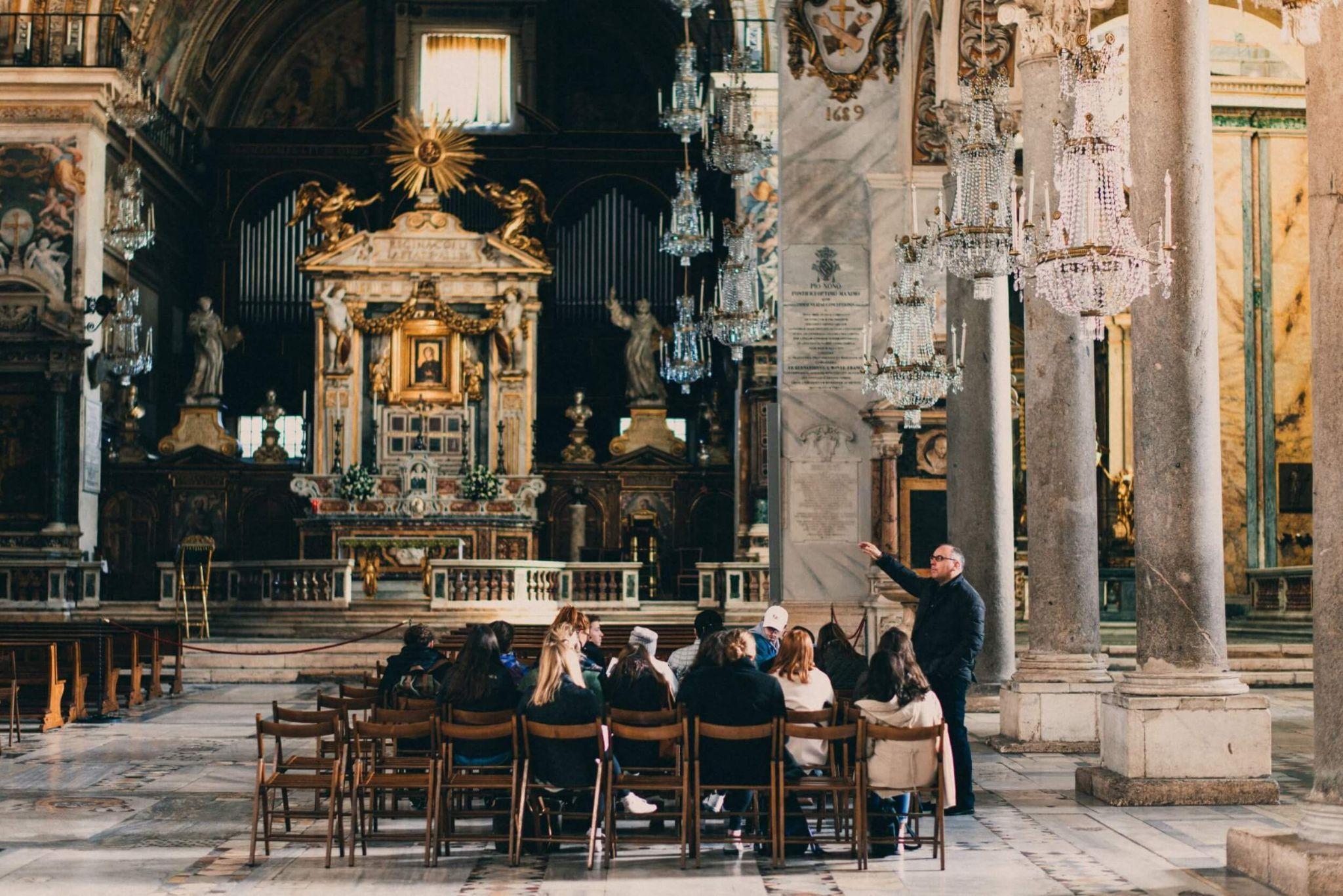 A class of students attending university in Rome listening to a lecture in an old church