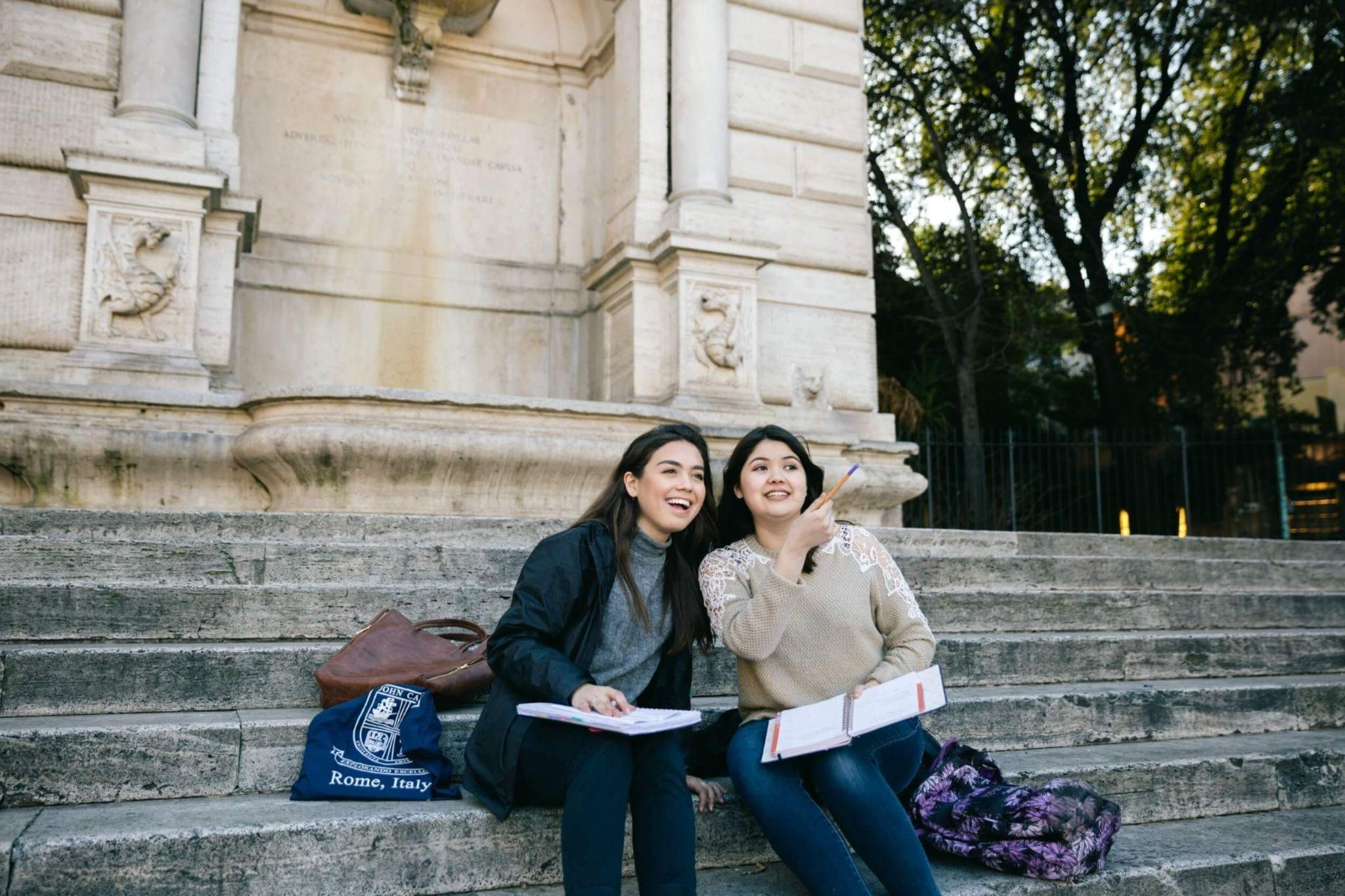 A pair of smiling students sitting on a step as they study abroad in Rome.