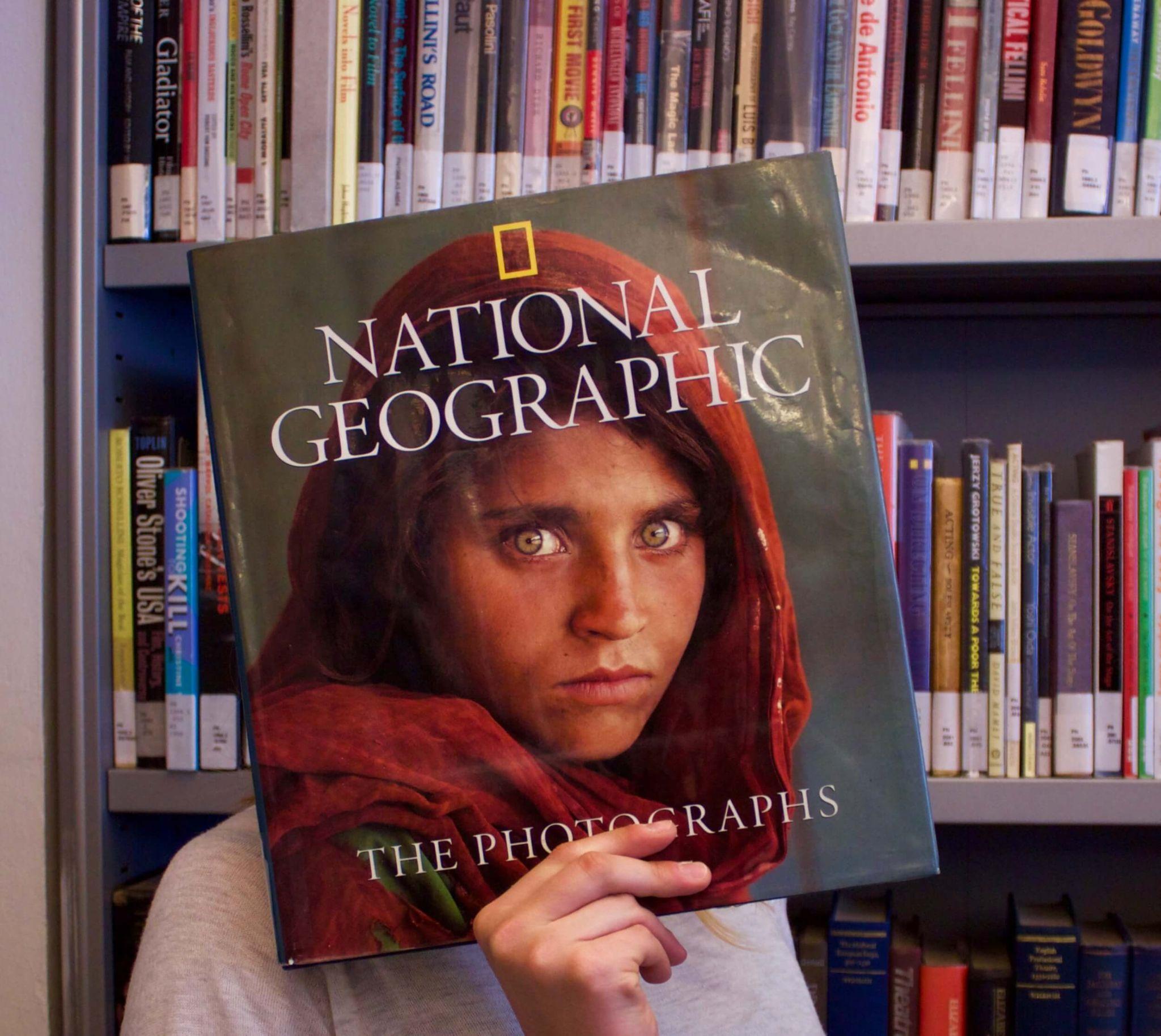 A female student with a major in business holding up a national geographic magazine in the school library