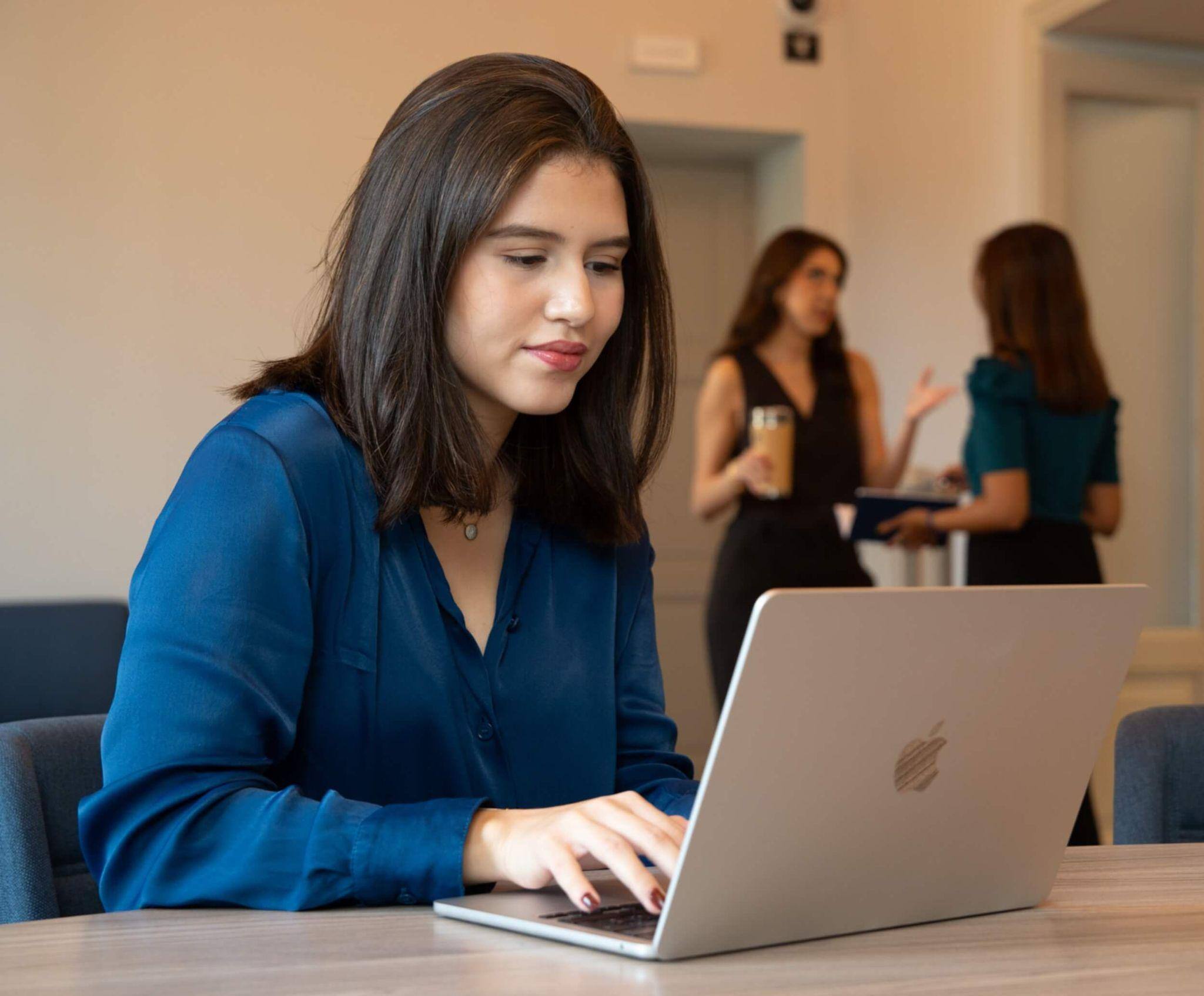 A focused female communications degree program undergraduate working on her computer in class