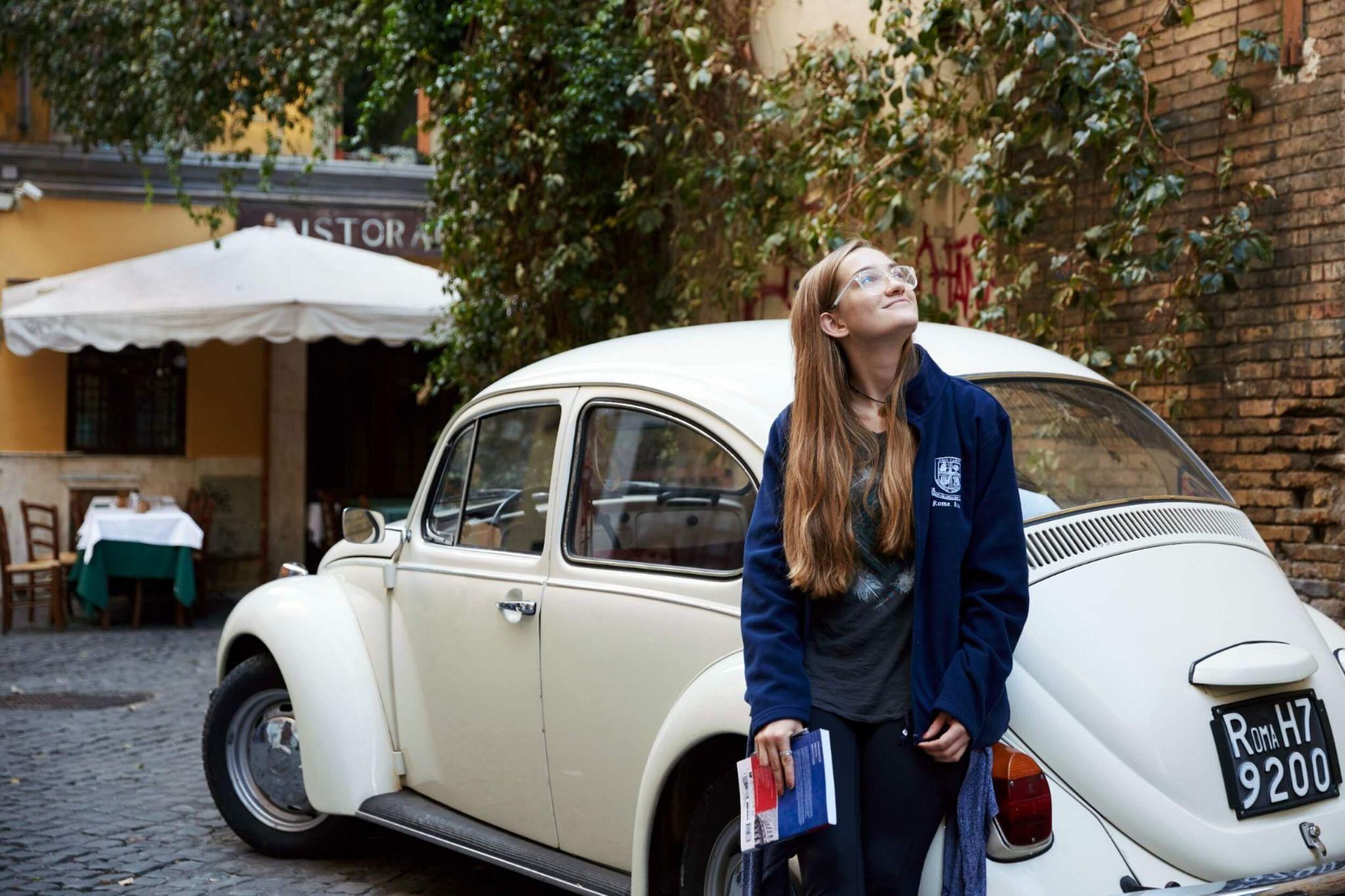 A student attending university in Rome posing in front of a vintage car