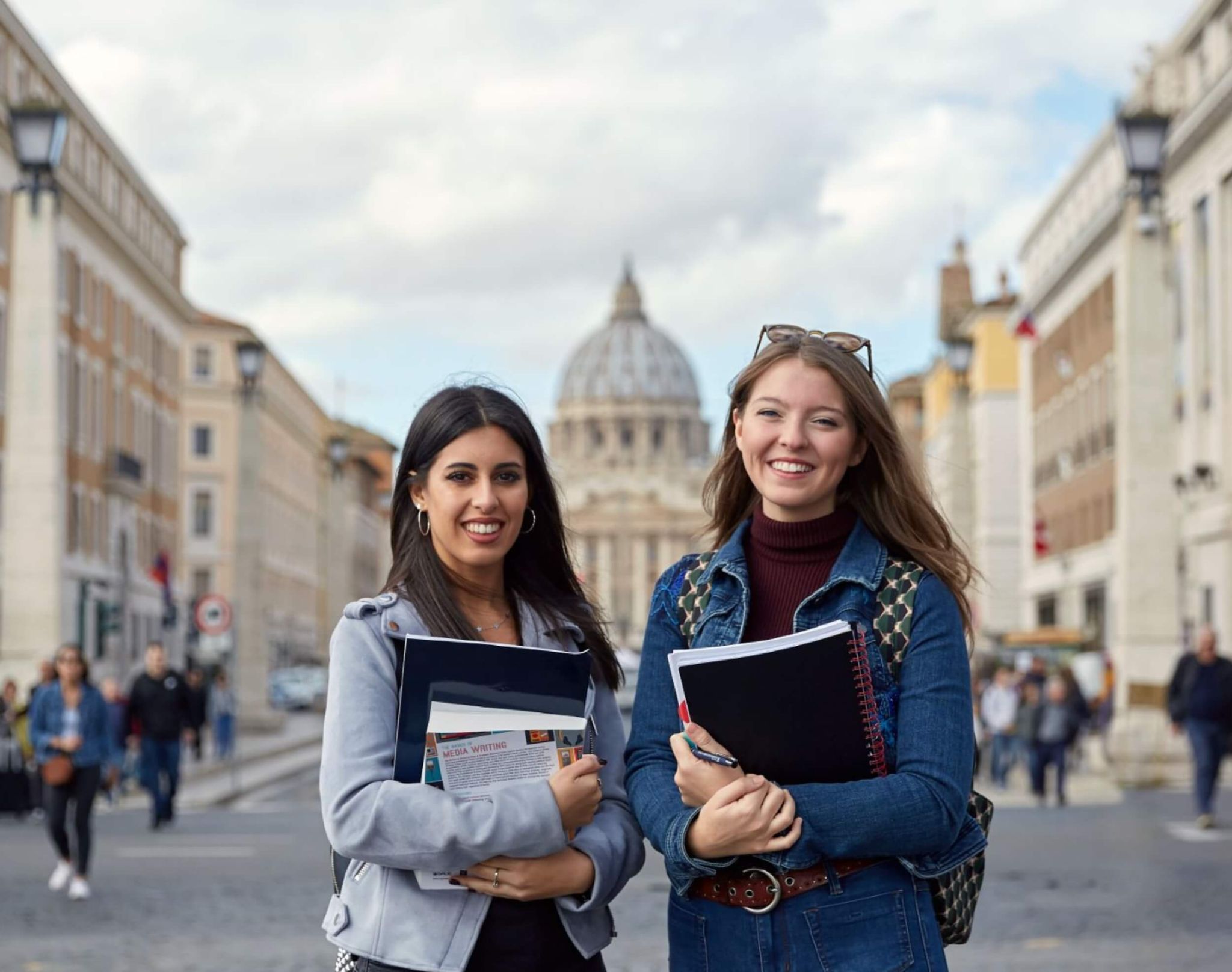 students attending university in Rome holding books and posing in front of a monument