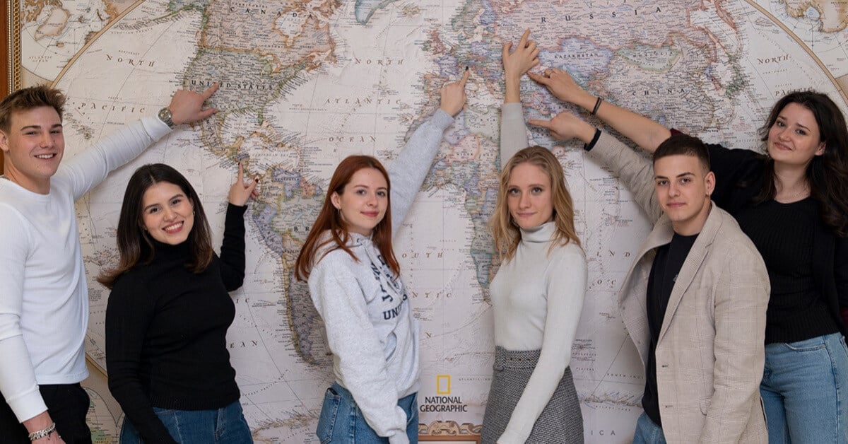 A group of smiling students pointing where they are from on the map