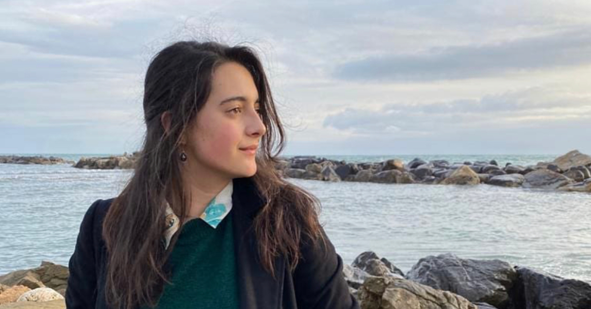 Girl staring off to the right side of the image in front of rocks and the sea