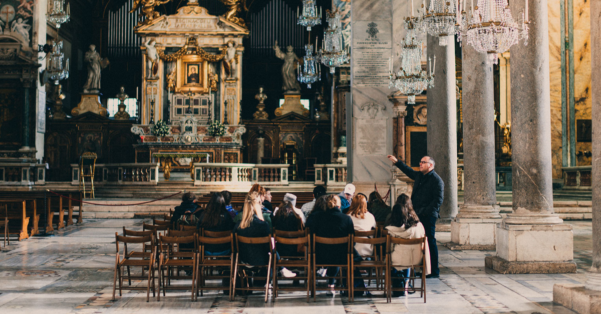 Students sitting in a church as professor explains the surroundings