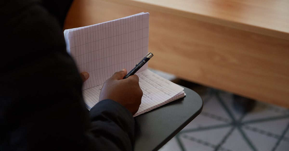 Student taking notes in a notebook with a John Cabot University pen.