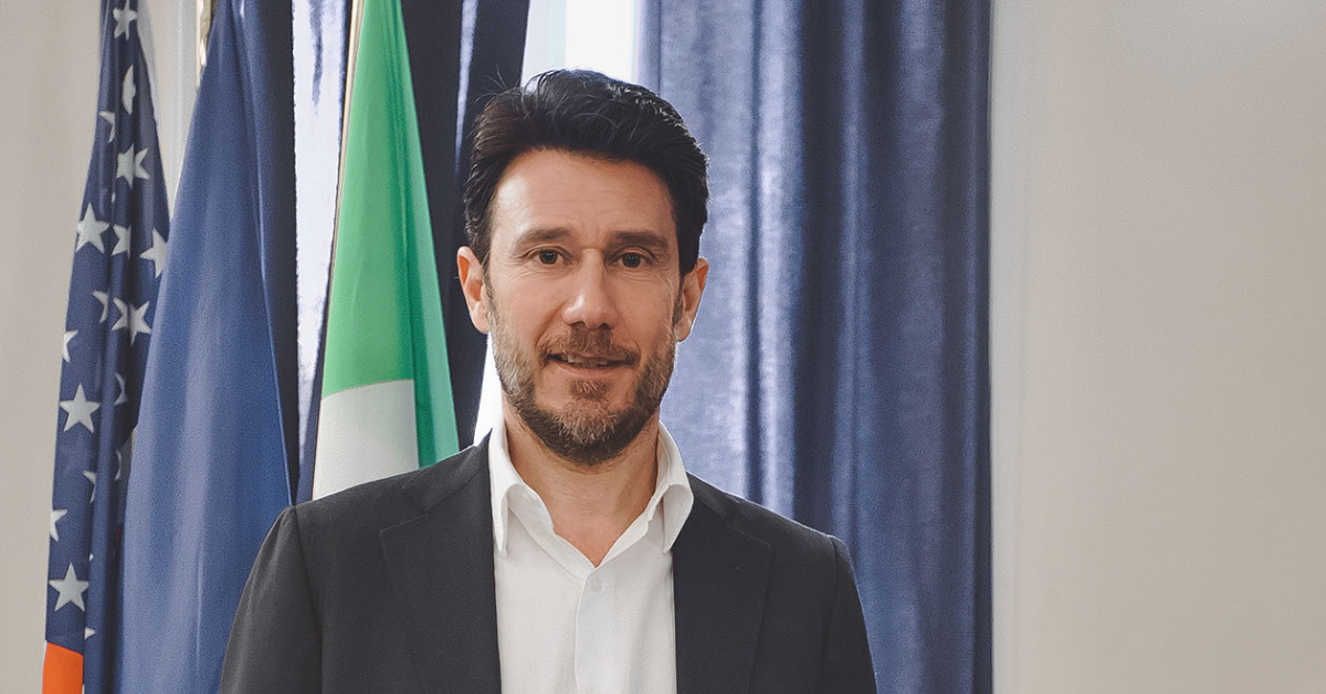 Uomo in posa davanti alle bandiere di Italia e Stati Uniti