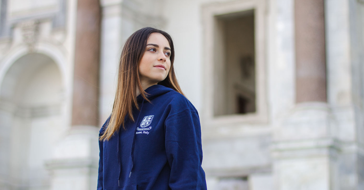Girl staring to the right side of the image wearing a John Cabot University sweater.