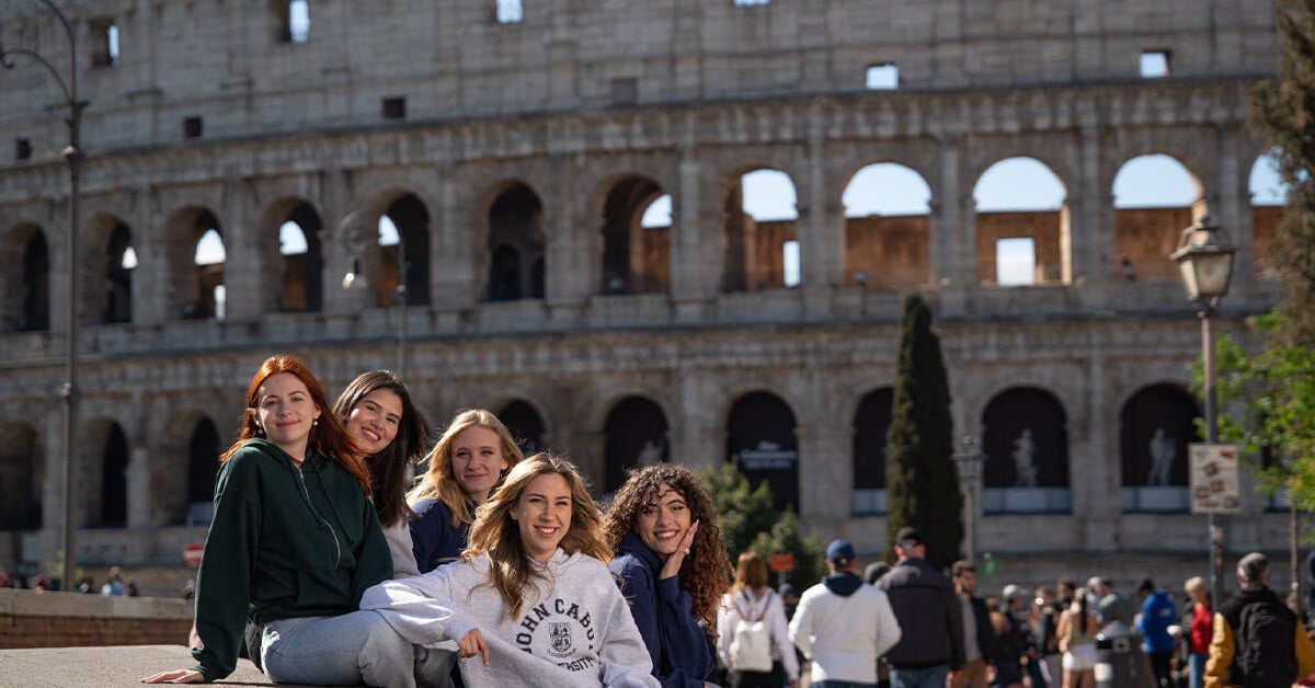 A group of diverse students gathered in an outdoor courtyard at John Cabot University in Rome, enjoying the vibrant atmosphere of studying abroad in Italy.