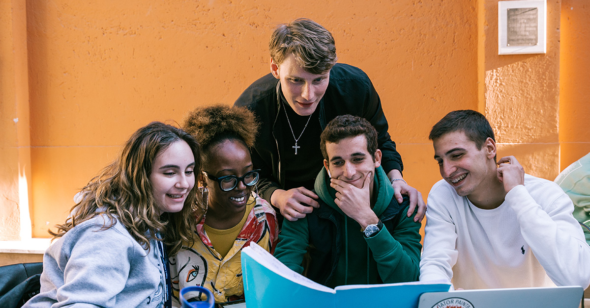 John Cabot students smile while working on a laptop on campus.